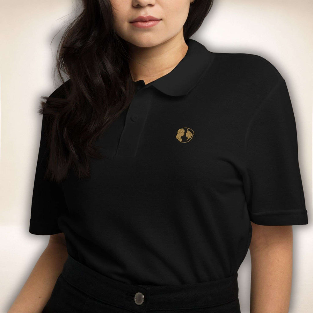 Schwarzes Belgravia Polo mit goldenem Doppelprofil-Logo, von einer Frau getragen