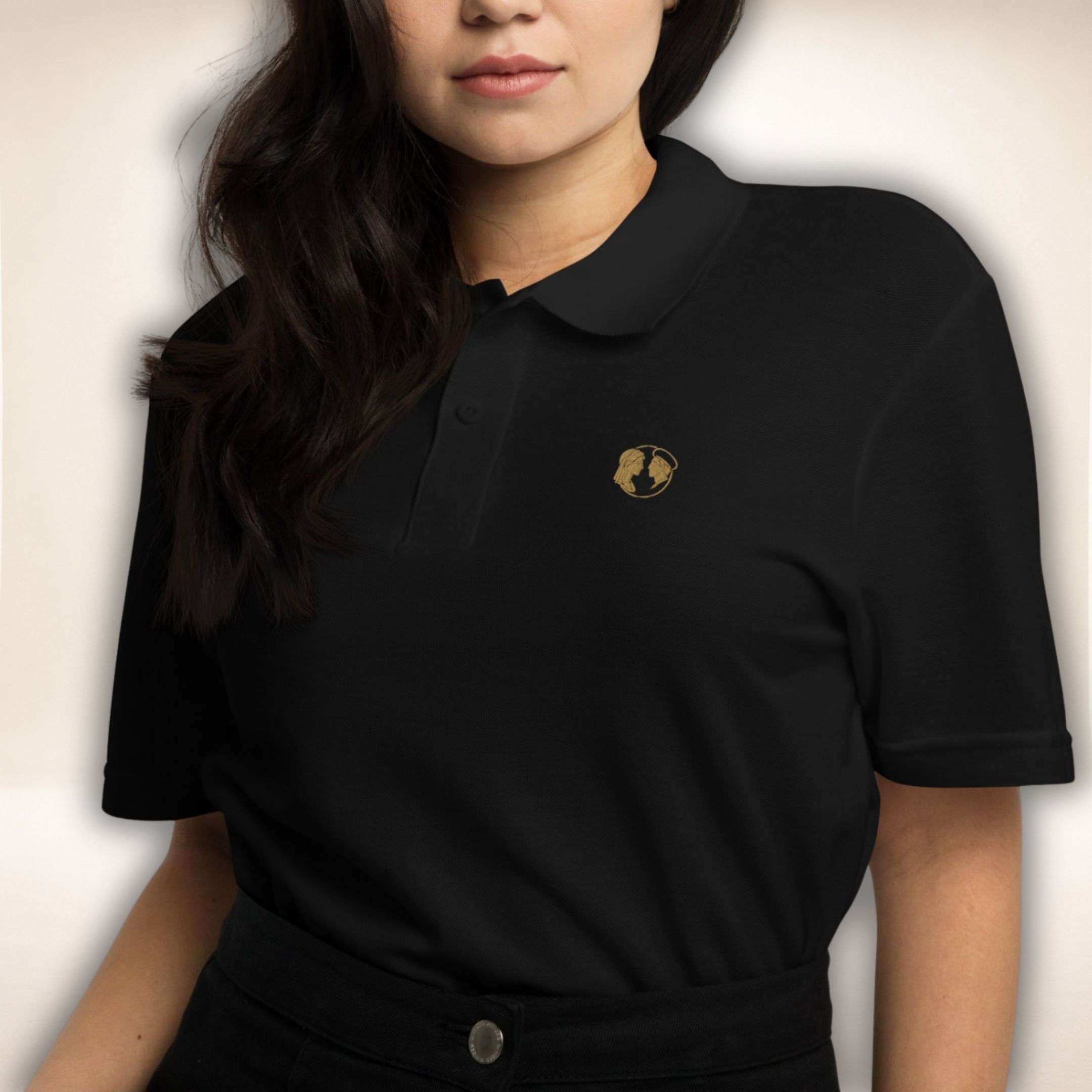 Schwarzes Belgravia Polo mit goldenem Doppelprofil-Logo, von einer Frau getragen